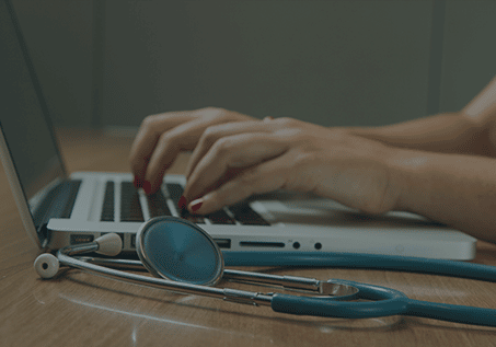 person typing on a laptop with a stethoscope on the table