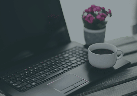 coffee cup sitting on the edge of an open laptop